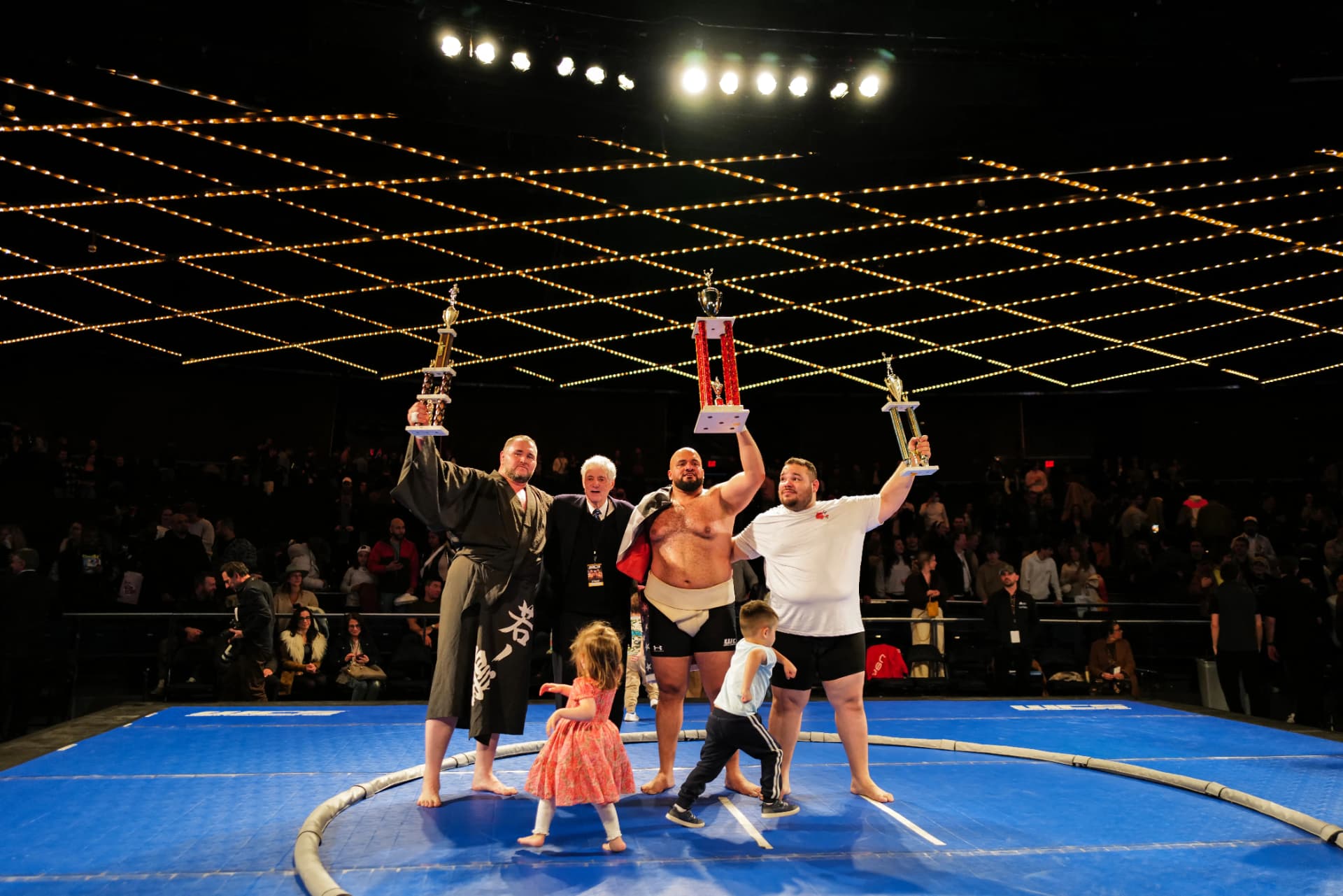 Podium finishers holding their trophies in the ring
