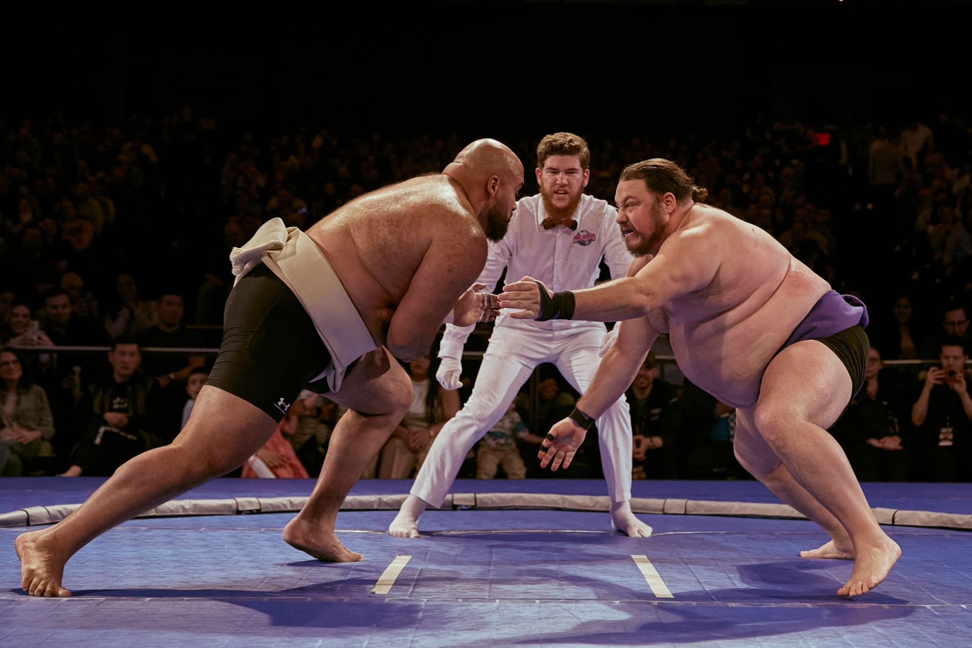 Two rikishi locked up at the tachiai as the referee watches
